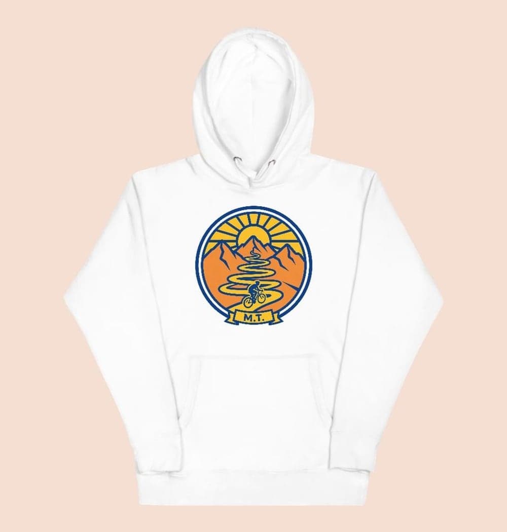 An original crest showing a cyclist riding toward a mountain pass, with a curving trail and rising sun, on a hoodie (example made with AI)